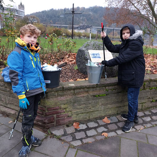 Zwei Jungen in Winterjacken an einer Mauer, sie haben Müll gesammelt