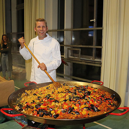 Hausmeister rührt in einer großen Paella-Pfanne
