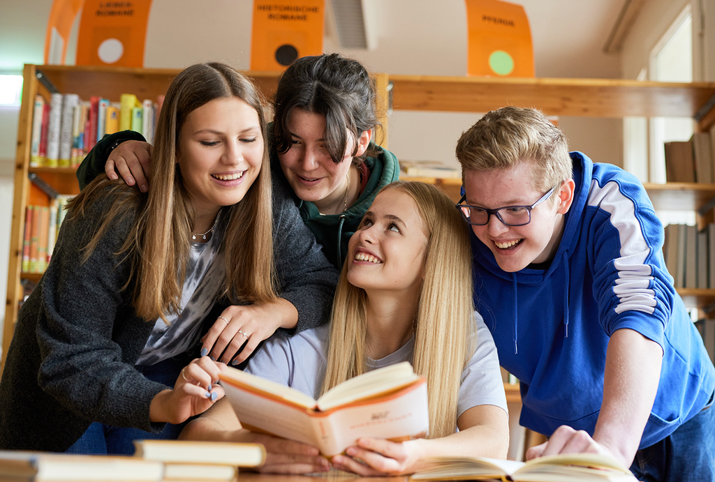 Vier Schüler und Schülerinnen informieren sich in einer Bibliothek